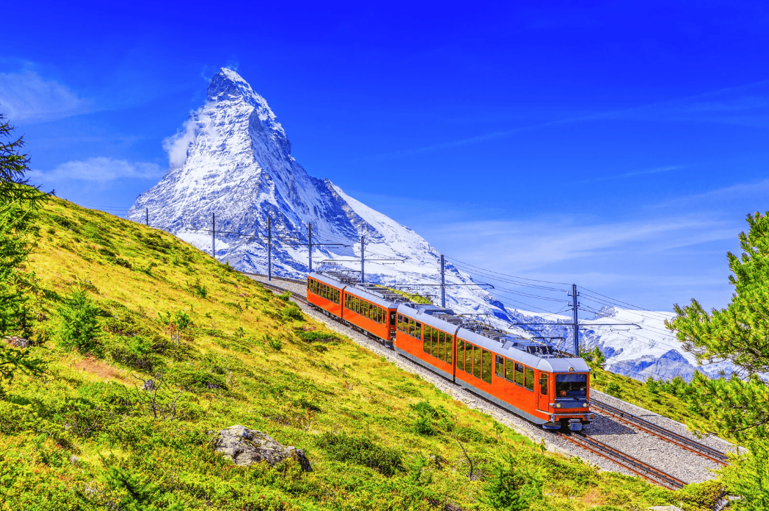 Mountain railroad travels through a green landscape with a view of the Matterhorn in Switzerland.
