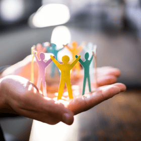 Hand holds colorful paper figures, symbolizing team spirit and employer attractiveness.