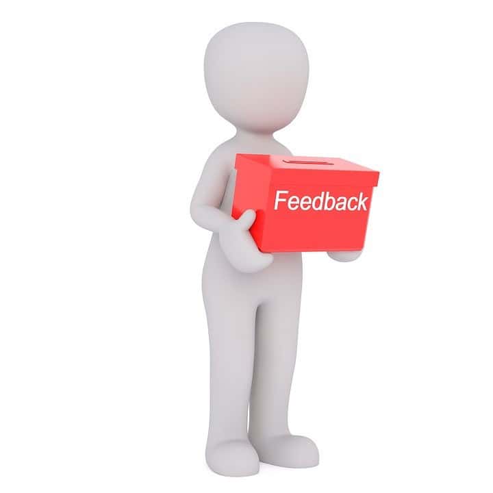 Figur hält eine rote Feedback-Box für kontinuierliches Feedback und Verbesserung.